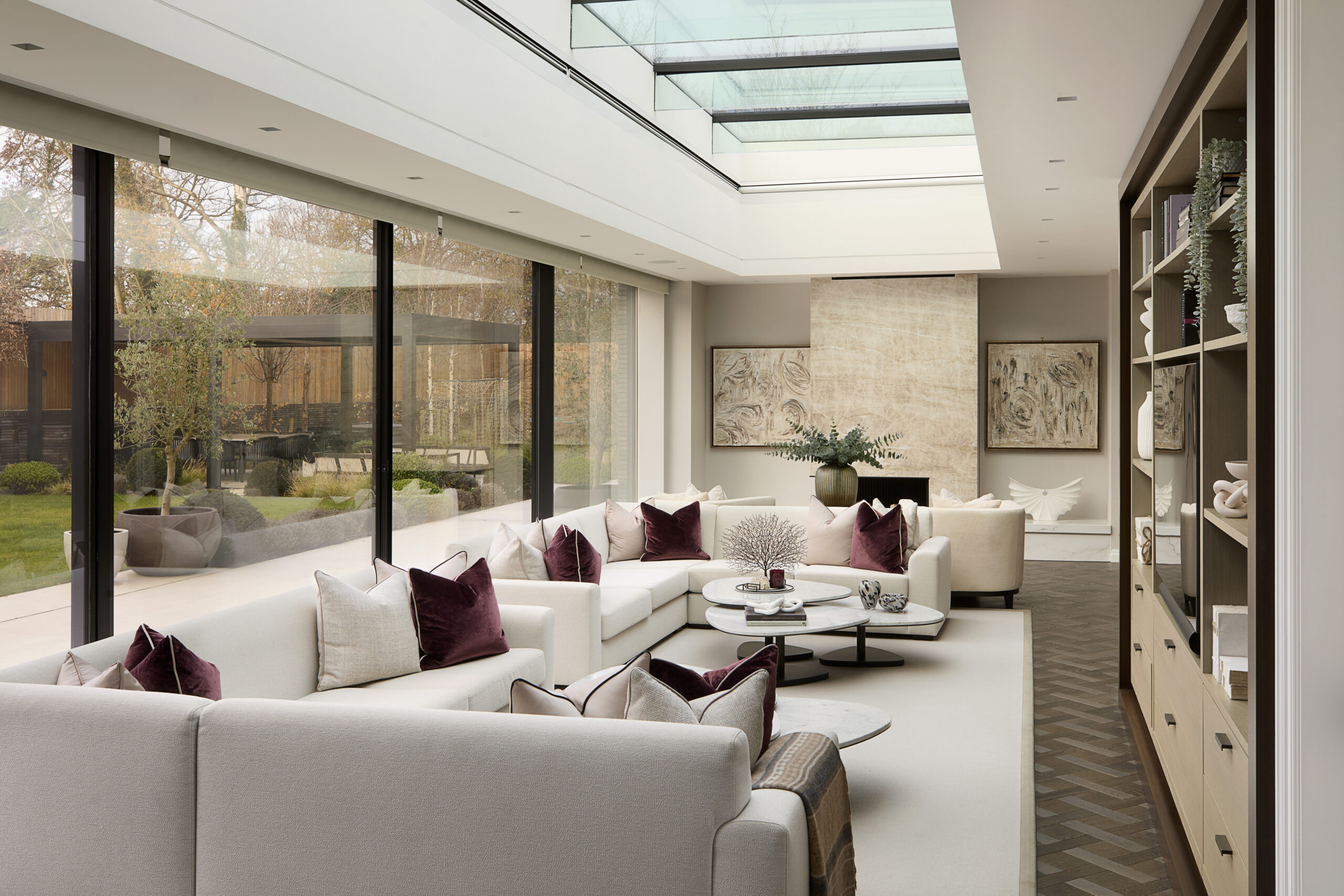 Cream colour sofa in a luxurious living room with dark red cushions and a coffee table made of marble styled with candles, trays and decorative objects